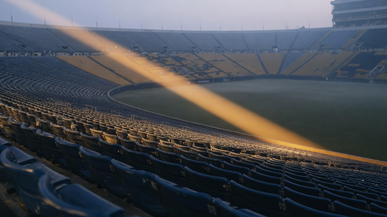 Empty college football stadium at first light, low fog over the field, warm amber sunlight cutting across navy seats.